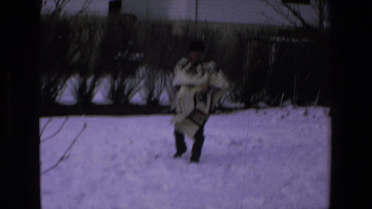 Adult man in a white poncho with dark geometric patterning and a dark hat walks across snow in 1972 8mm home-movie footage labeled Mazatlan, Mexico.