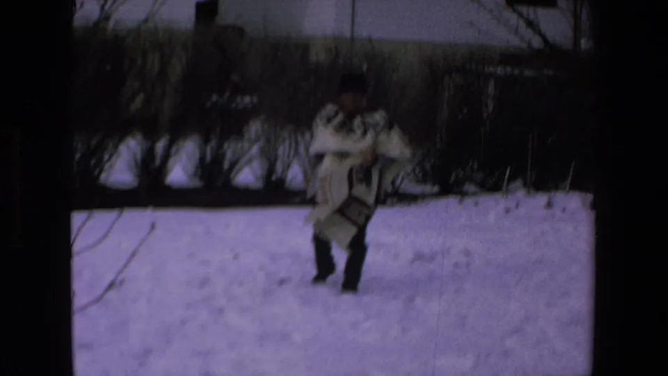 Adult man in a white poncho with dark geometric patterning and a dark hat walks across snow in 1972 8mm home-movie footage labeled Mazatlan, Mexico.