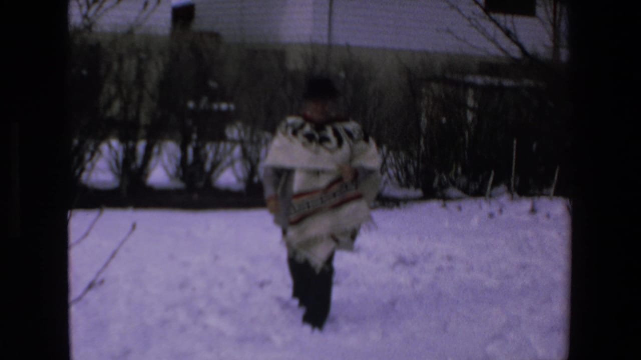 Man in a patterned poncho walking away across a snowy yard.
