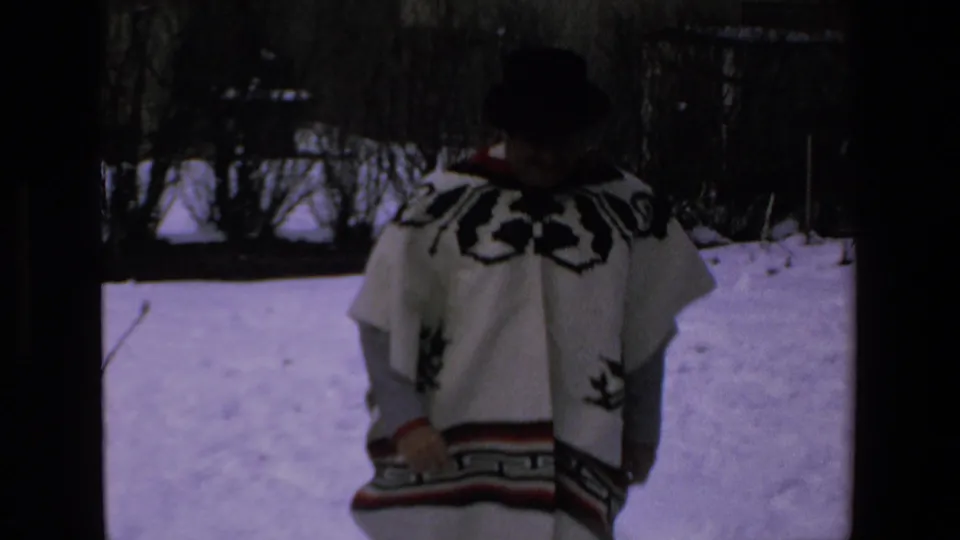 An adult man wearing a dark hat and white woven poncho with black patterns stands in a snowy outdoor yard in footage identified by metadata as Mazatlan, Mexico, 1972.