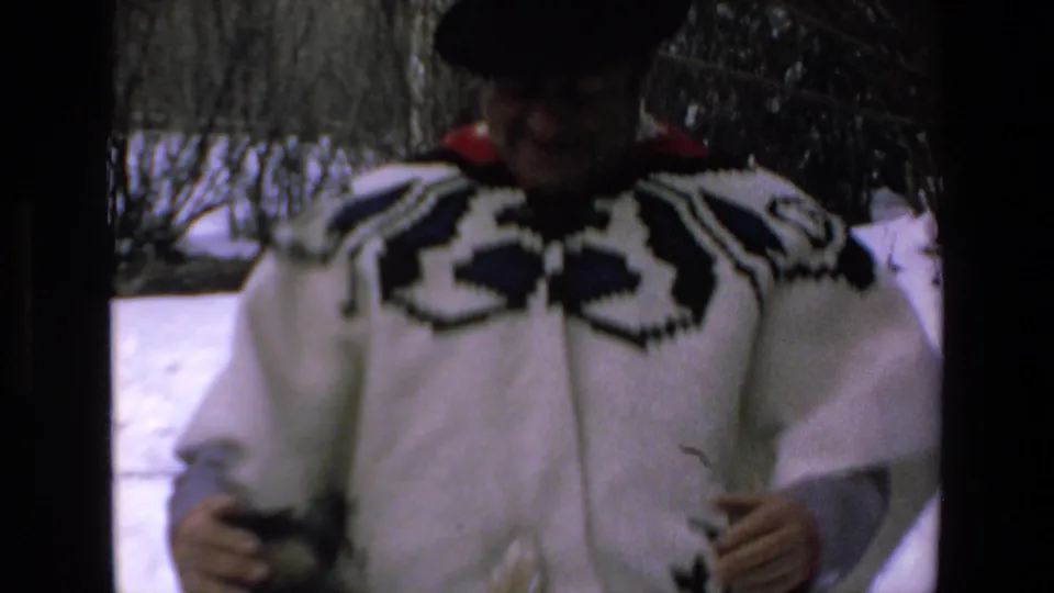 A closer 8mm frame shows the adult man approaching the camera in a white patterned poncho, dark hat, and layered clothing against a snowy outdoor background.
