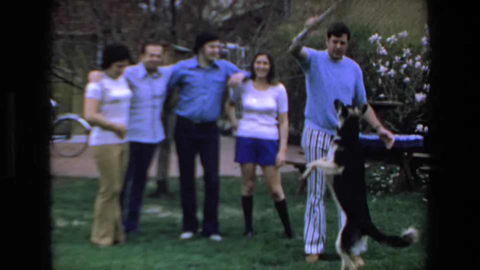 In the final frame, the dog reaches upward toward a raised stick as the man steps beside it and the adults remain grouped in the 1972 Mazatlan lawn scene.