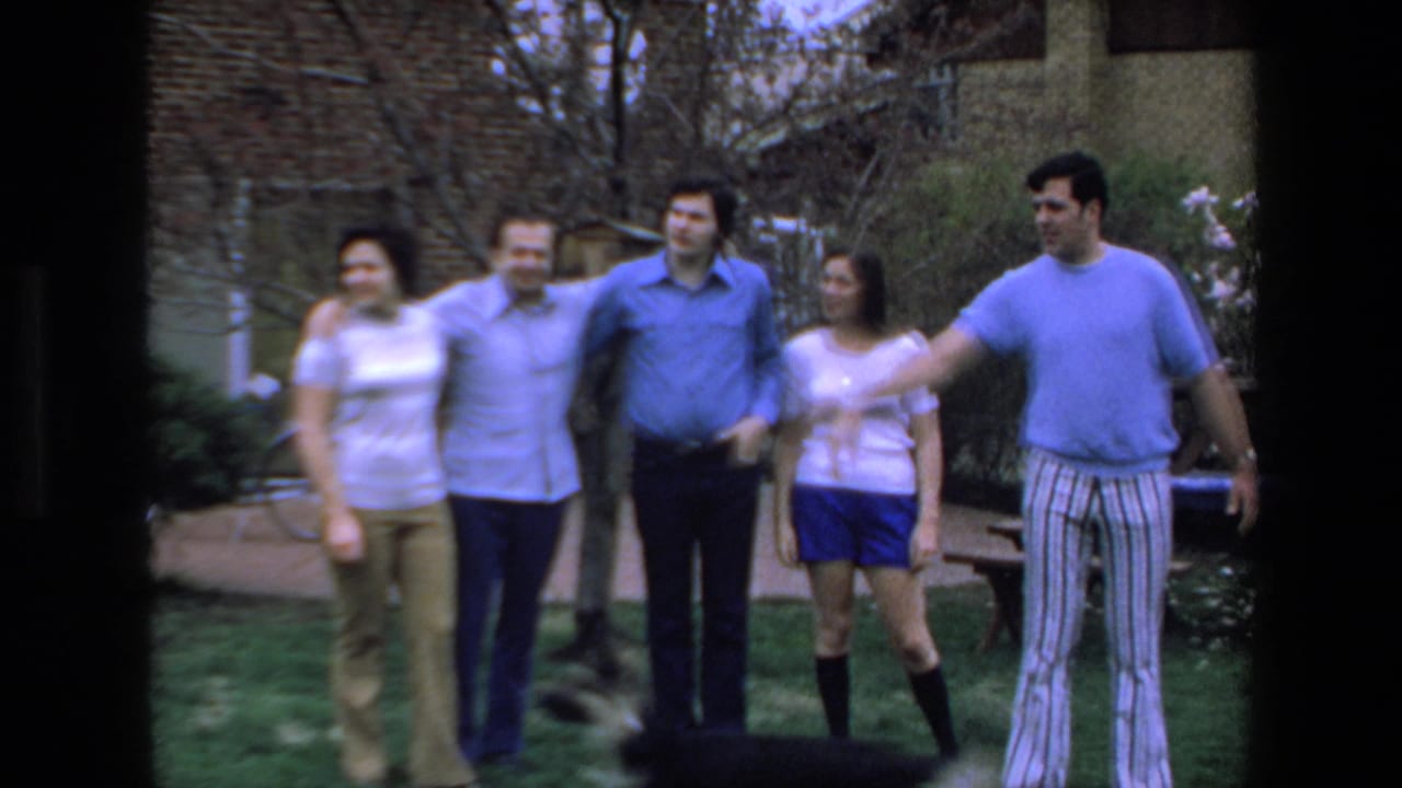 A group of adults stands together on grass as a man extends his arm near a dog.