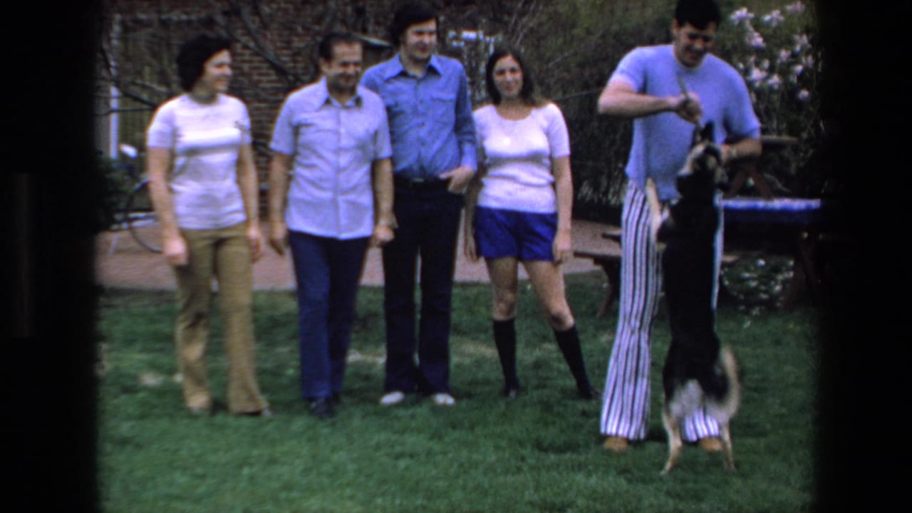 Four adults stand smiling as a man at right plays with a dog on a grassy lawn.