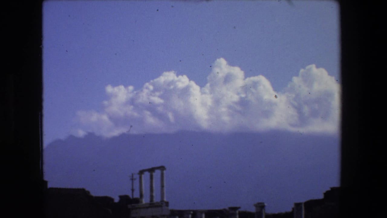 Distant hills and clouds above low ruins and column fragments.
