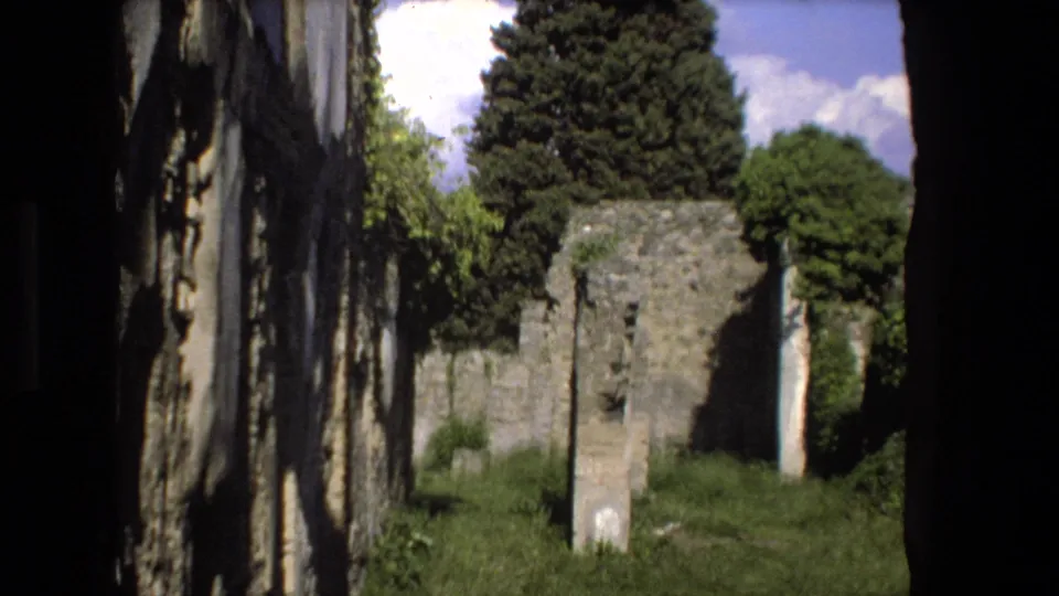 1973 Rome home-movie frame showing weathered stone ruins, grass, trees, and deep foreground shadow around a historic site view.