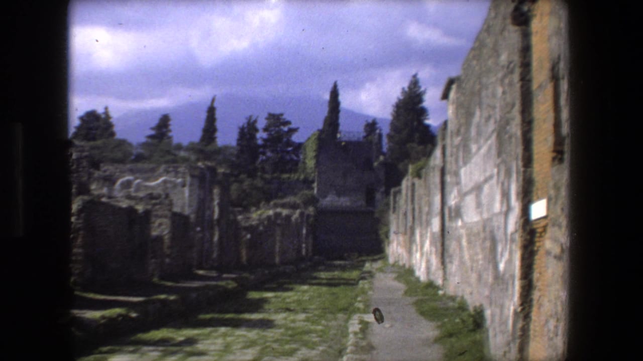 Narrow walkway beside ruined stone walls under a cloudy sky.