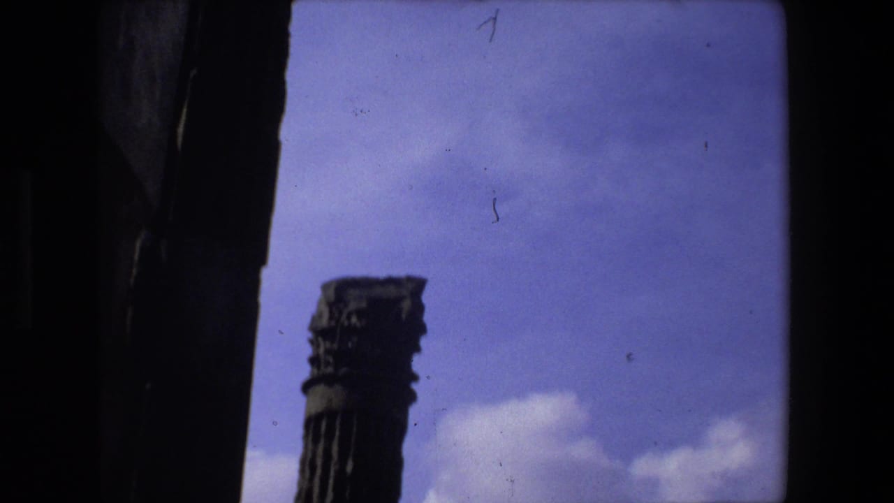 1973 Rome 8mm frame showing a weathered ancient column with a carved capital, partially enclosed by dark architectural edges and sky.