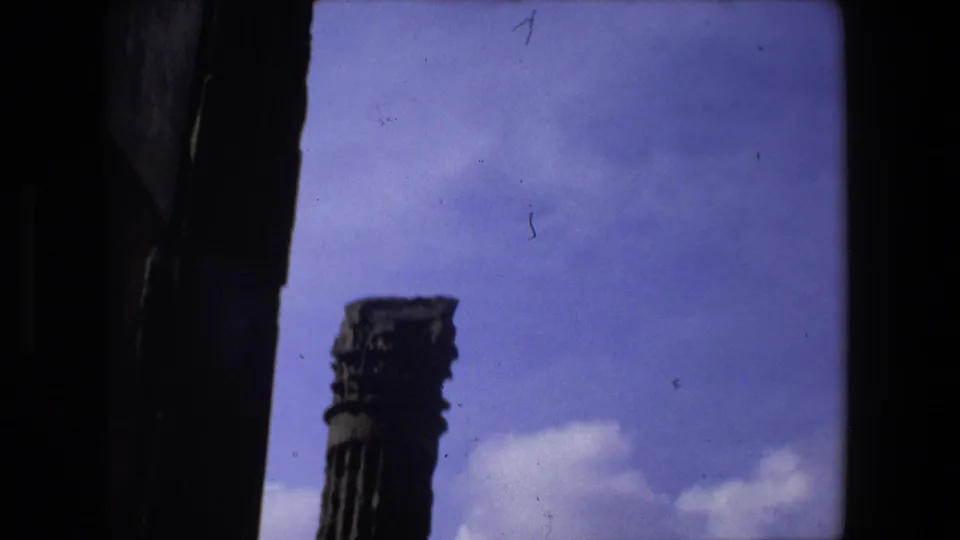 1973 Rome 8mm frame showing a weathered ancient column with a carved capital, partially enclosed by dark architectural edges and sky.