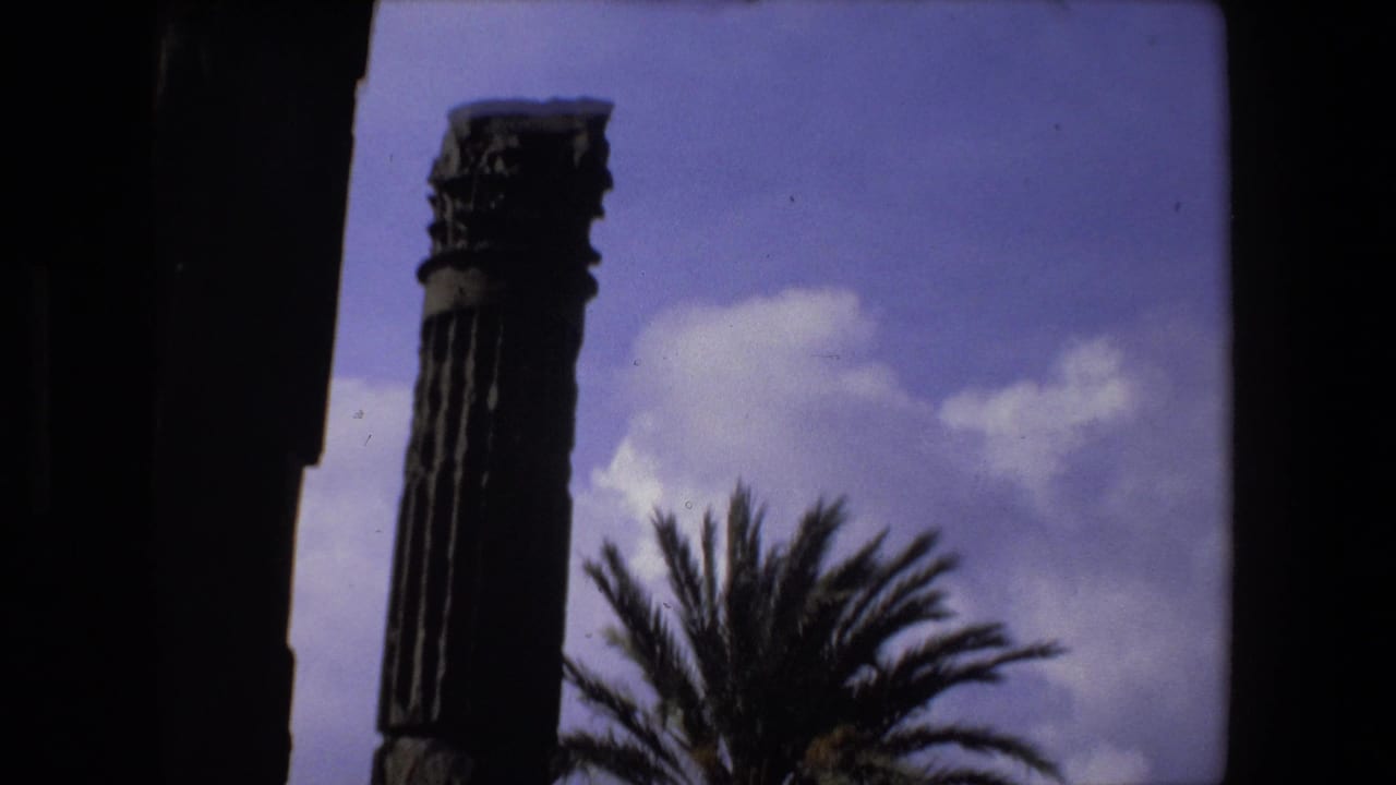 1973 Rome 8mm frame with a tall ancient column, palm fronds, partial ruin walls, and a blue-purple sky with clouds.