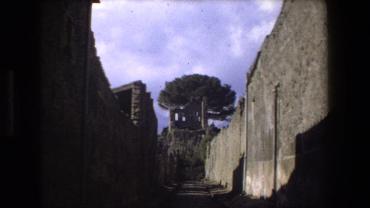 1973 Rome travel footage frame showing a narrow walled passage between ancient masonry, with a tree and broken structure visible in the distance.