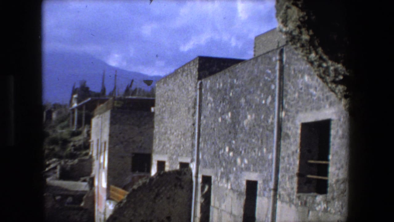1973 Rome home-movie frame showing rough stone walls, dark window openings, hillside greenery, and a blue sky at an ancient ruin site.