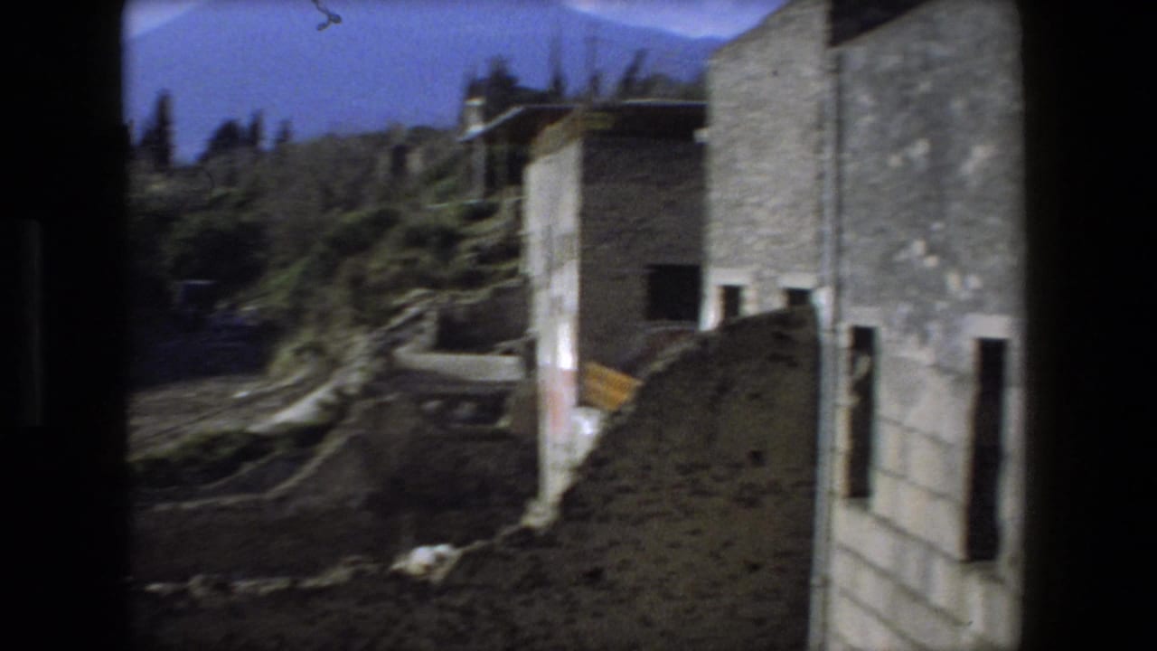 1973 Rome travel footage frame with stone structures, uneven earth, vegetation, and a partially visible path or terrace through the ruin area.