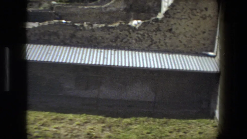 Rome, Italy 1973 home-movie frame showing a corrugated protective roof below exposed earth and grass at a historic excavation site.