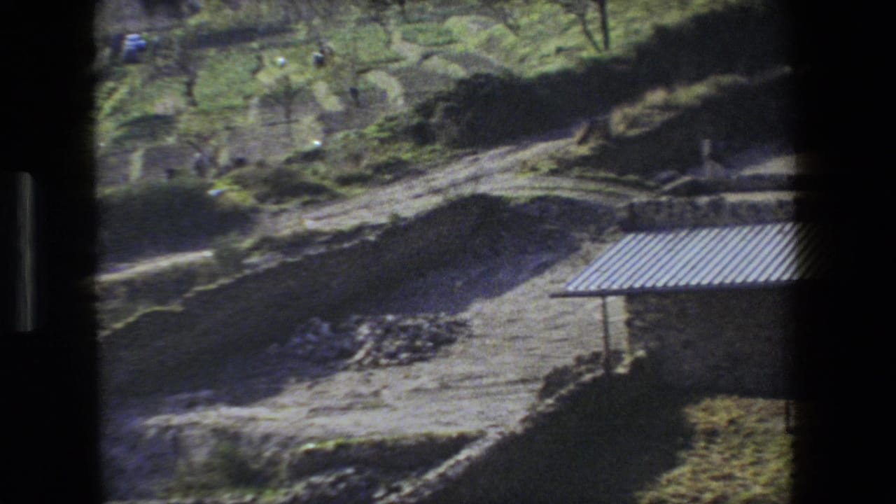 Excavated hillside with corrugated roof edge and small distant figures.