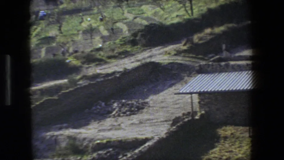 Rome, Italy 1973 frame looking across dirt mounds, stone remains, greenery, and small distant people near a partially excavated historic site.