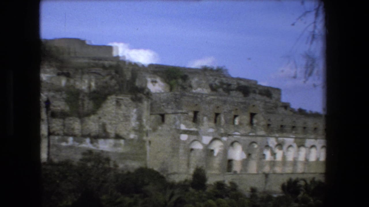 1973 Rome-area home-movie frame showing ancient-looking stone ruins with arched openings, scrub vegetation, and dark 8mm frame edges.