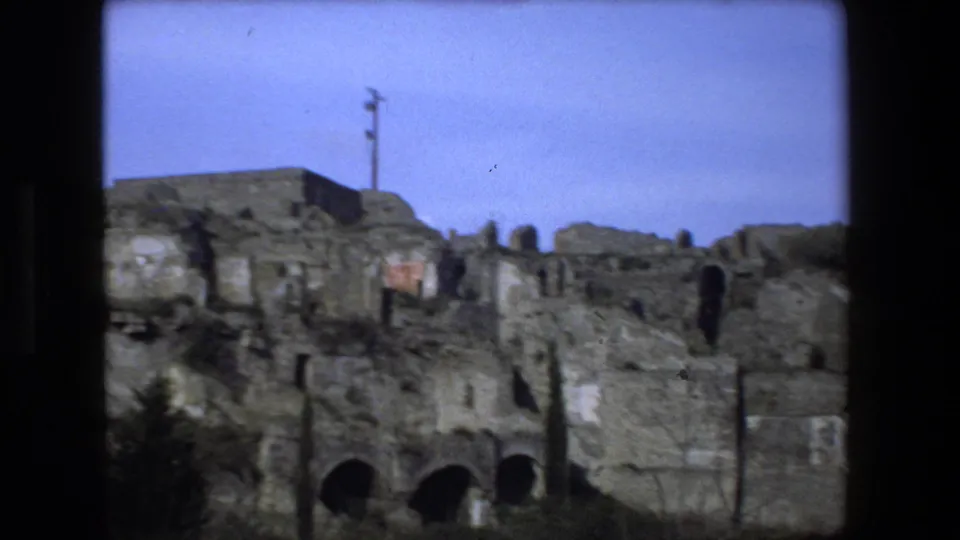1973 Rome-area home-movie view of a ruin complex with arched lower openings, rough stone surfaces, and a small pole or mast above the upper wall.