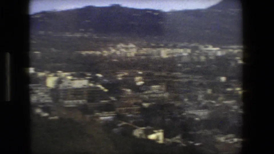Grainy 1973 8mm travel frame showing a high-angle view over Rome's urban landscape with hills beyond, seen through dark film-frame edges.