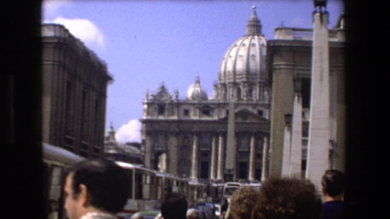 1973 Rome home-movie frame of tourists near St. Peter's Basilica, with the dome, facade, colonnade, obelisk, and heads of visitors in the foreground.