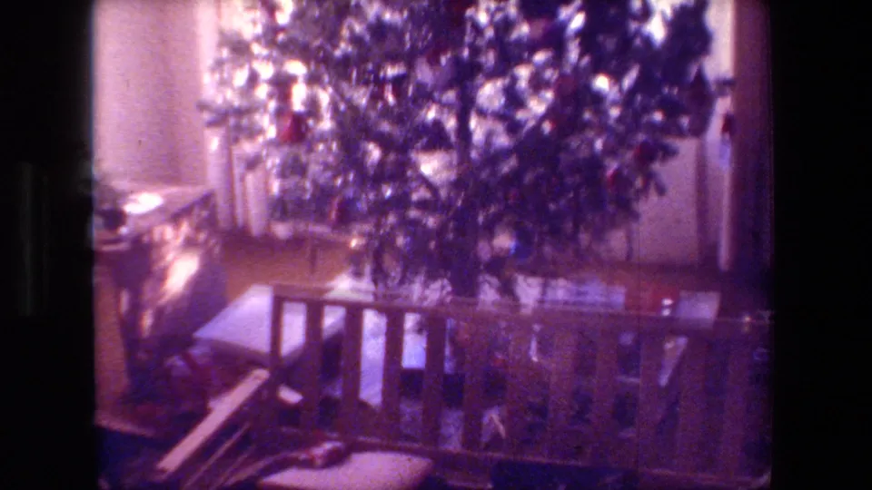 The final frame shows the Christmas tree, gifts beneath it, window curtains, and a wooden bench or railing, with the soft grain and color shift of 8mm film.