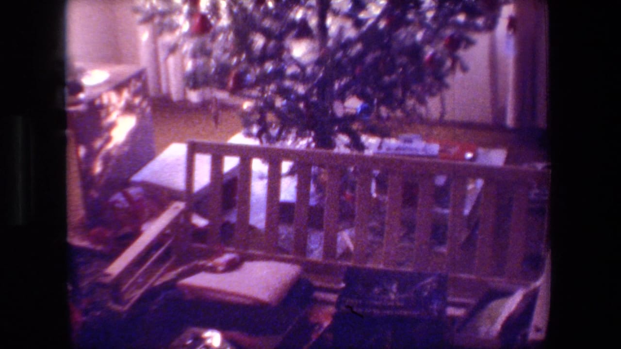 Dim living room corner with a decorated Christmas tree, wooden bench, cushion, and boxes.