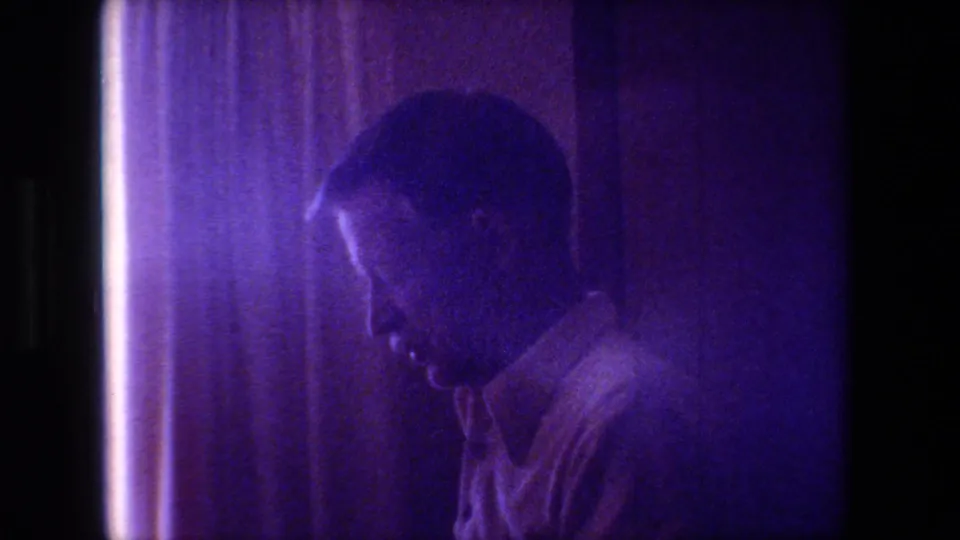 An adult man, likely the father described in the clip metadata, appears in profile beside curtains in the 1981 Hollywood, California home-movie Christmas interior.