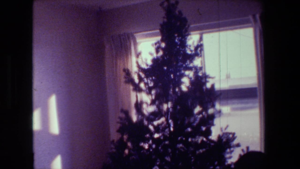 1981 Hollywood home-movie frame with a Christmas tree silhouetted against a curtained window inside a private room.