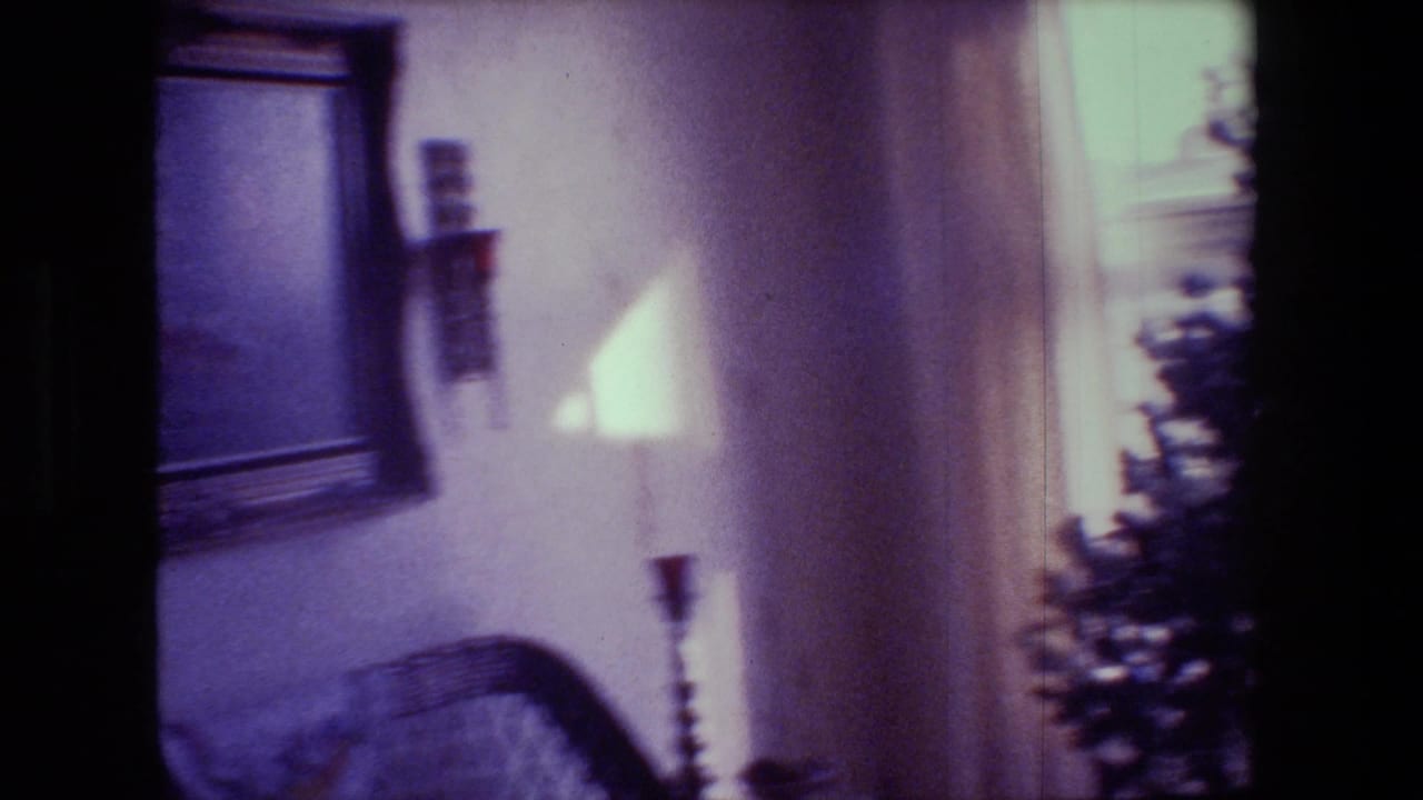 1981 Hollywood, California home-movie frame with framed wall art, candle fixtures, bright window light, and the edge of a Christmas tree inside a private living room.