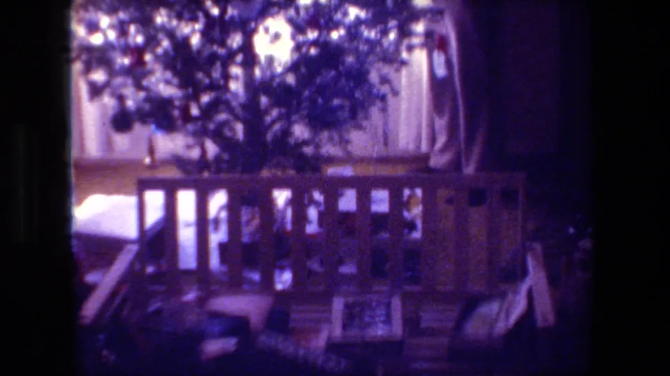1981 Hollywood, California home-movie frame showing a decorated Christmas tree behind a wooden railing, with curtains and living-room furnishings in soft 8mm light.