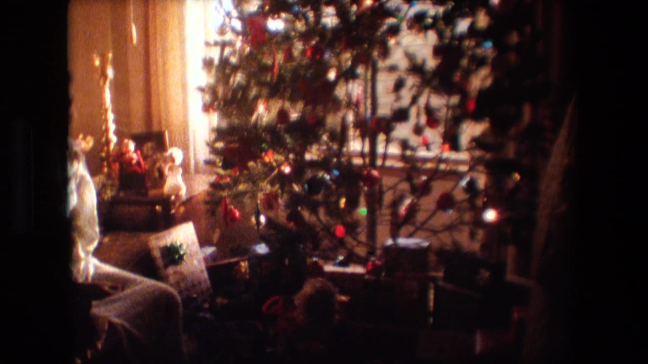 A Lansing, Michigan 1981 home-movie frame shows a decorated Christmas tree, wrapped presents, tinsel, and household furnishings in a warm private living room.