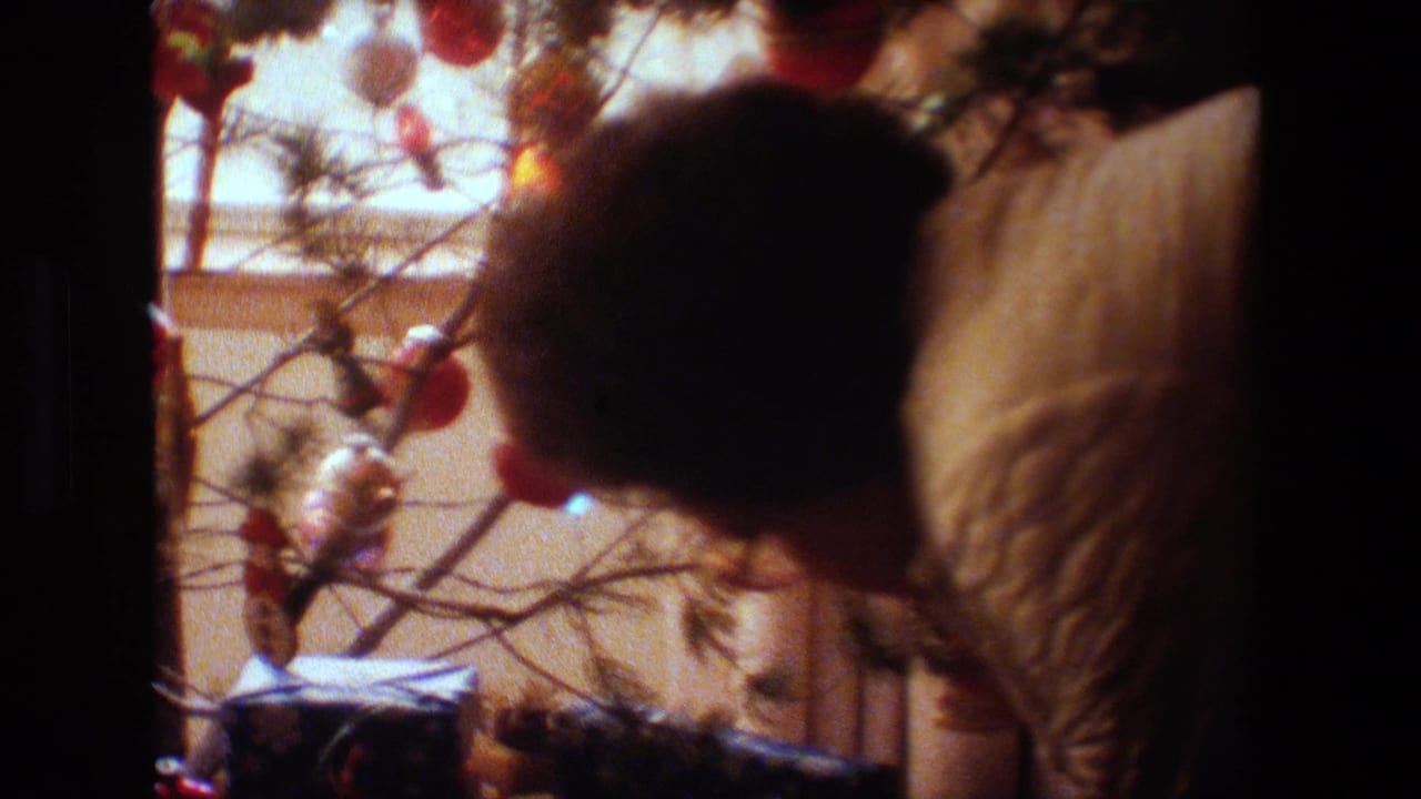 Person in a quilted jacket bends close to a decorated Christmas tree.