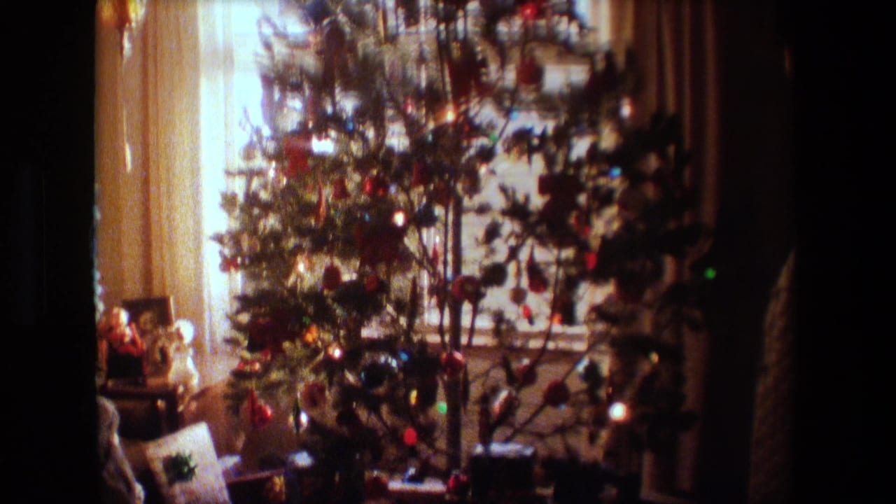 1981 Lansing, Michigan home-movie frame showing a decorated indoor Christmas tree in front of bright sheer-curtained windows, with small objects near the base.