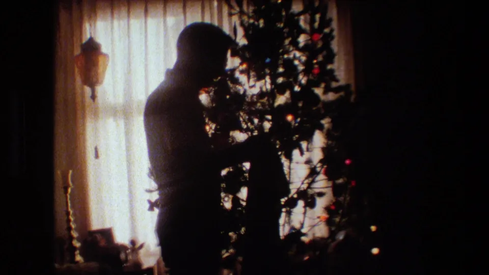 The silhouetted man appears to handle or adjust something on the Christmas tree in a warmly backlit 1981 Lansing home interior.