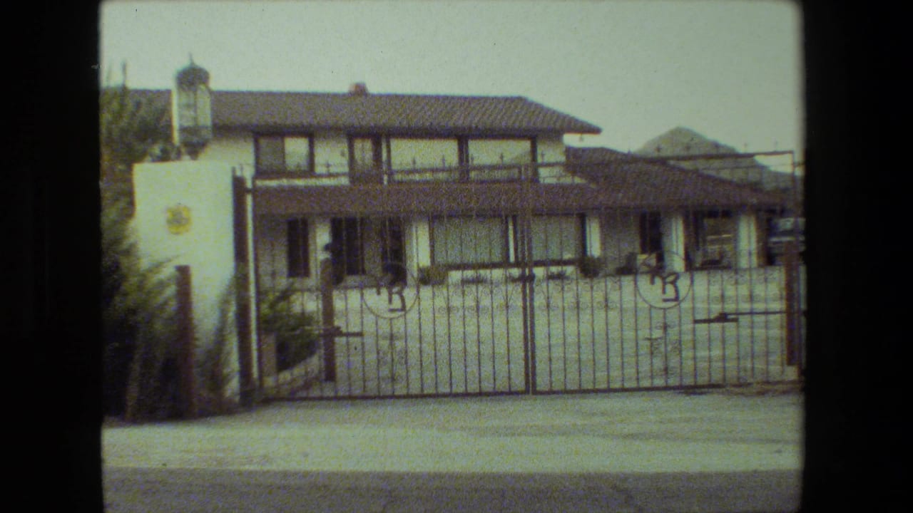 Two-story stucco house behind a metal driveway gate with circular emblems.