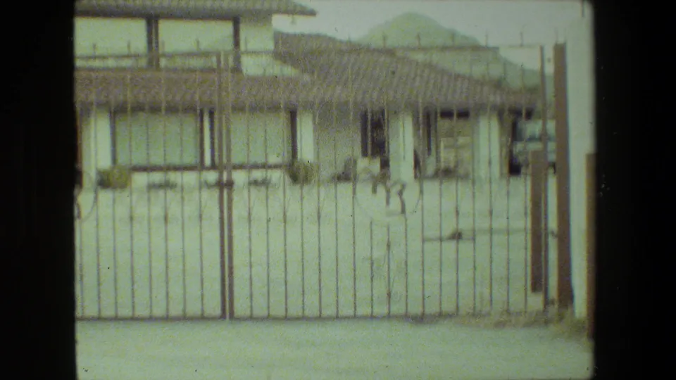 Soft 8mm frame from Malibu in 1981 showing the gated residential exterior, stucco walls, rooflines, windows, and driveway foreground.