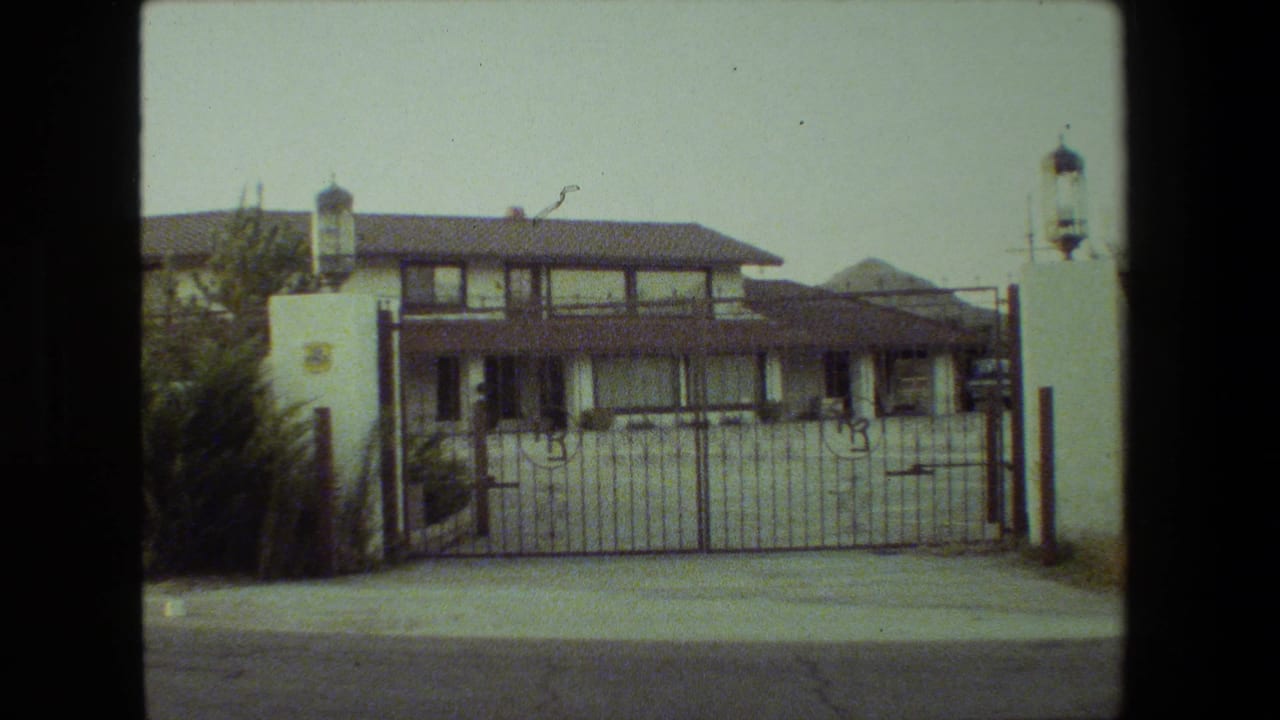 Two-story house and metal gate framed by white pillars and landscaping.