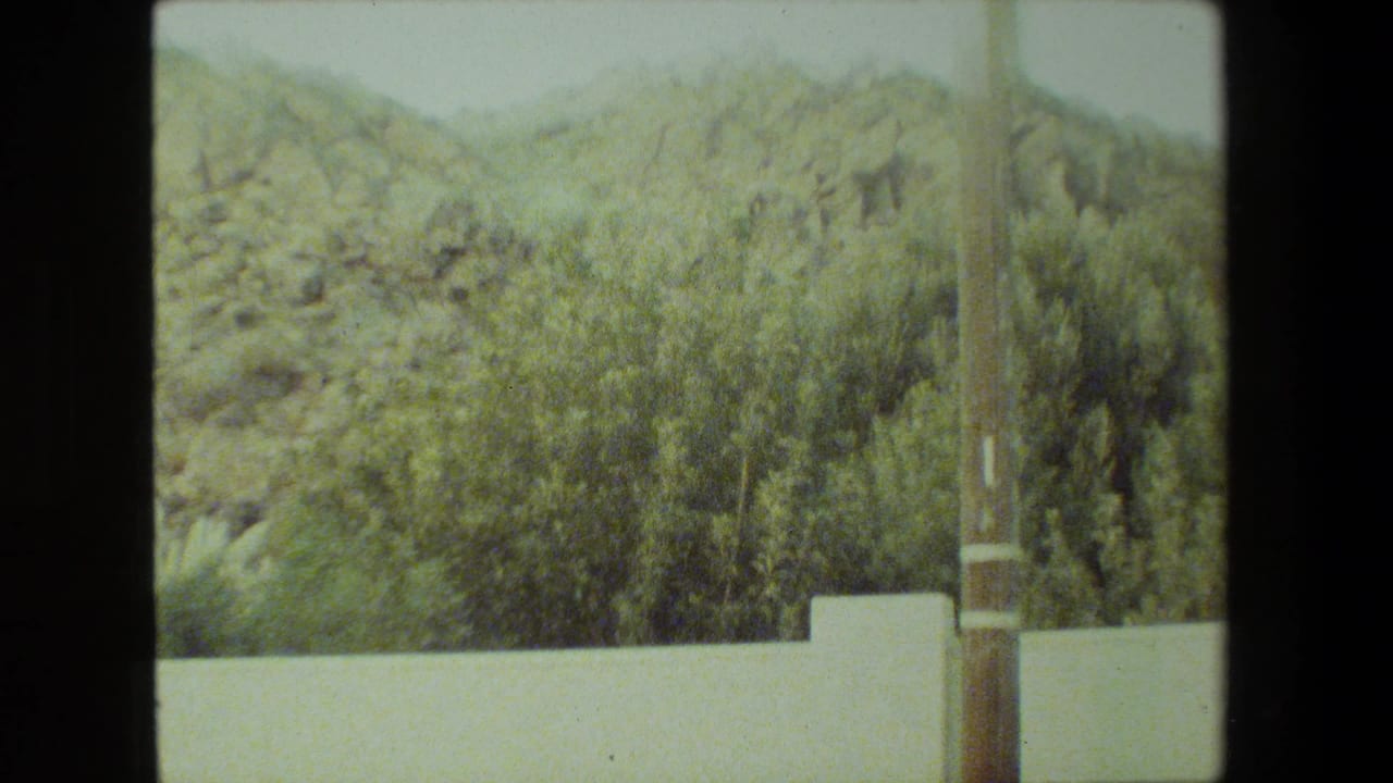 Rocky hillside and shrubs behind a white wall with a utility pole at the right.