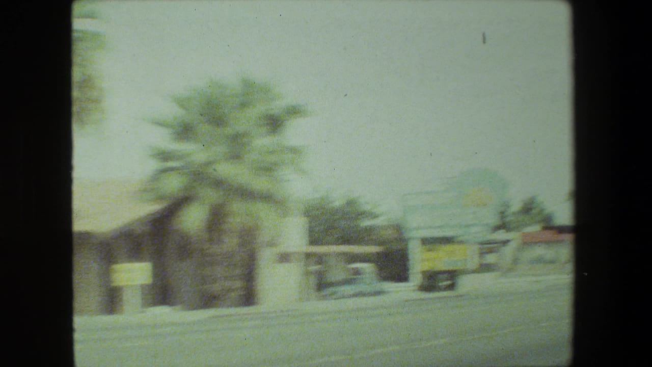 Faded 8mm view of a Malibu, California roadside with palm trees, low commercial buildings, and a broad street during a 1981 family road trip.