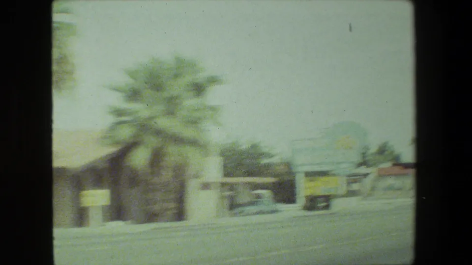 Faded 8mm view of a Malibu, California roadside with palm trees, low commercial buildings, and a broad street during a 1981 family road trip.