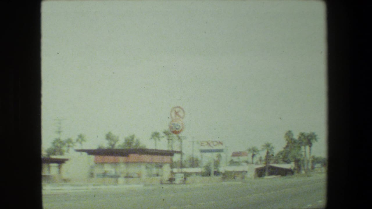 Roadside businesses with a distant Exxon sign and palm trees.