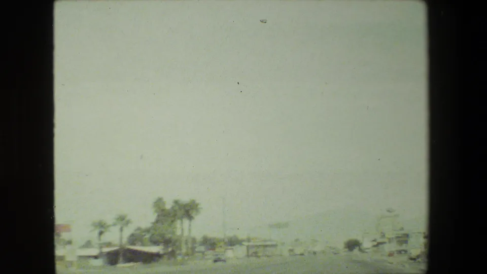 Washed-out 8mm road view from the Malibu, California trip, with palm trees, distant commercial buildings, and small cars visible along the street.