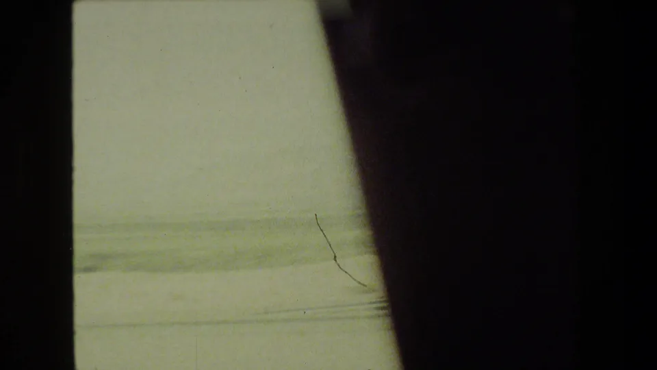 Hazy 1981 in-car 8mm view of open roadside terrain, with the vehicle window frame cutting through the scene.