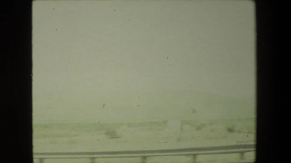 Small-gauge home-movie frame showing low roadside lines and pale terrain outside a moving vehicle in the 1981 Malibu clip metadata.