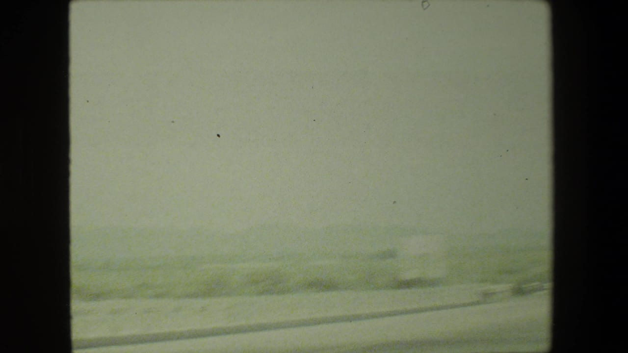 1981 Malibu home-movie frame showing a hazy moving-car view of a pale road curving through dry hills.