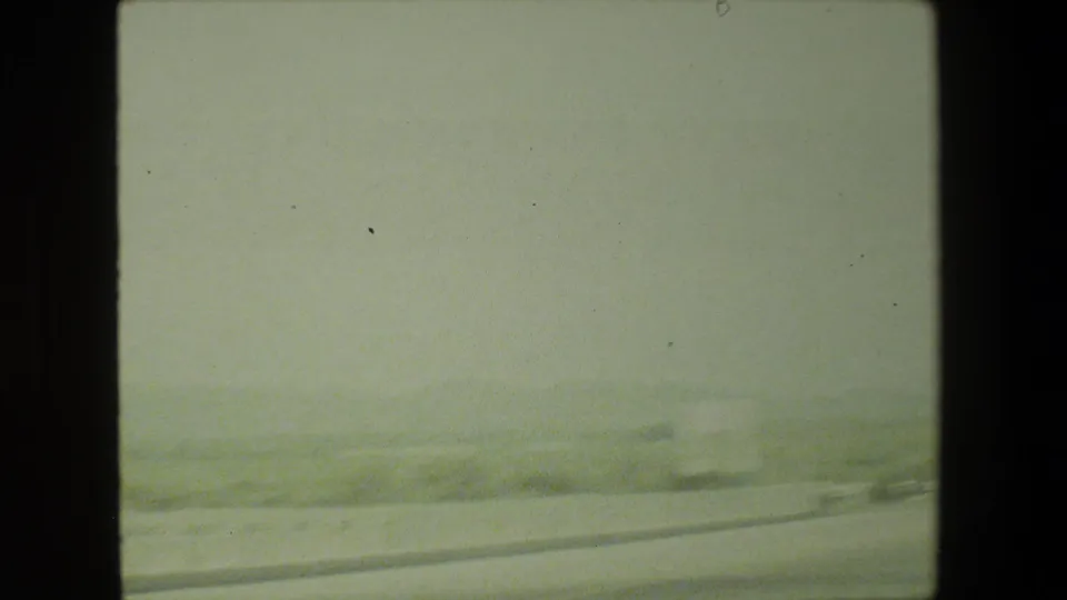 1981 Malibu home-movie frame showing a hazy moving-car view of a pale road curving through dry hills.