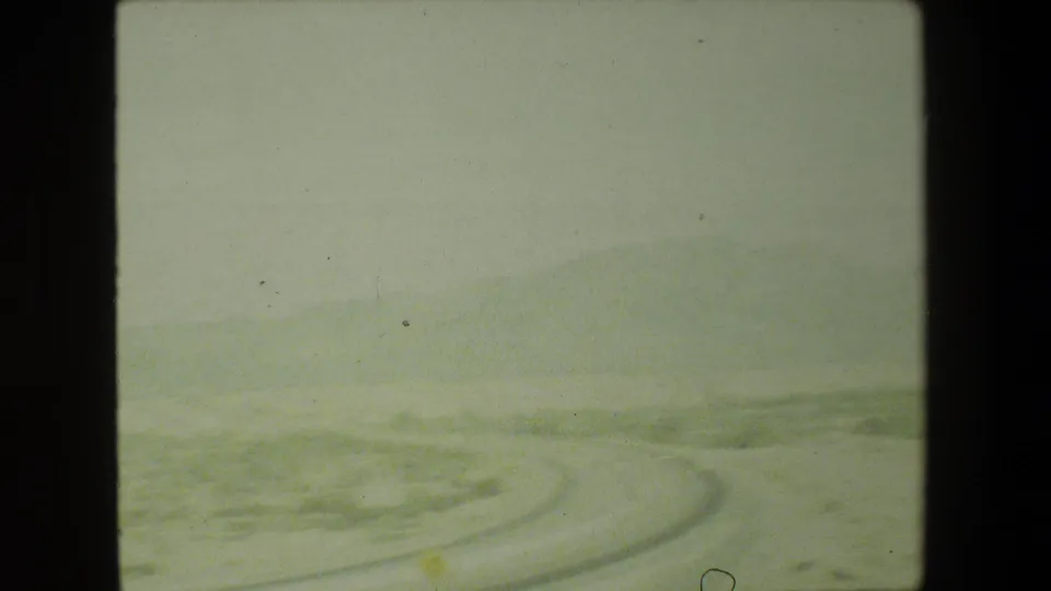 1981 Malibu 8mm frame with a soft, greenish view of a road bending across arid terrain and distant hills.