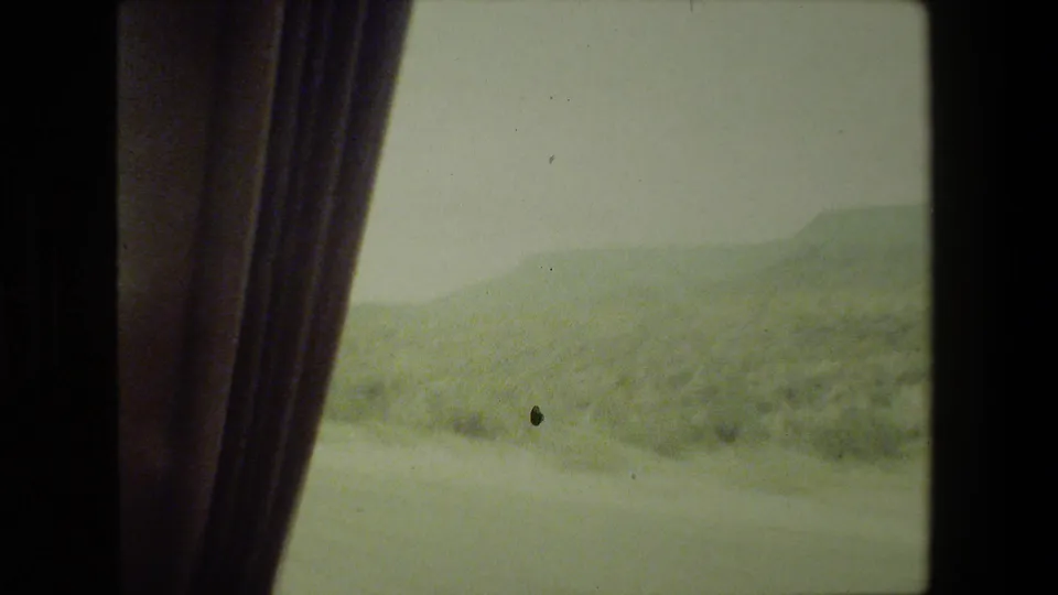 1981 Malibu 8mm frame showing dry hills through a vehicle window, partly obscured by a dark curtain or interior trim.