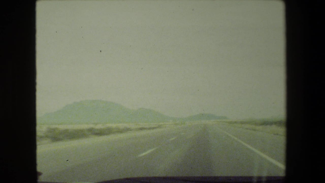1981 8mm view from a moving vehicle on a hazy highway near Malibu, California, with distant mountains and lane markings visible.