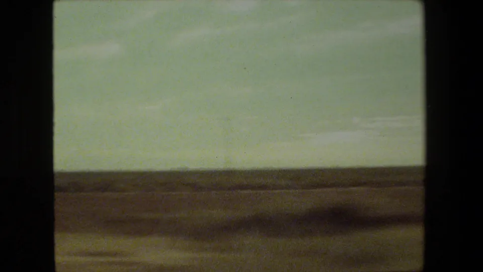 Moving-vehicle 8mm view of open Malibu-area roadside terrain, with a low horizon, hazy sky, and strong motion blur across the foreground.